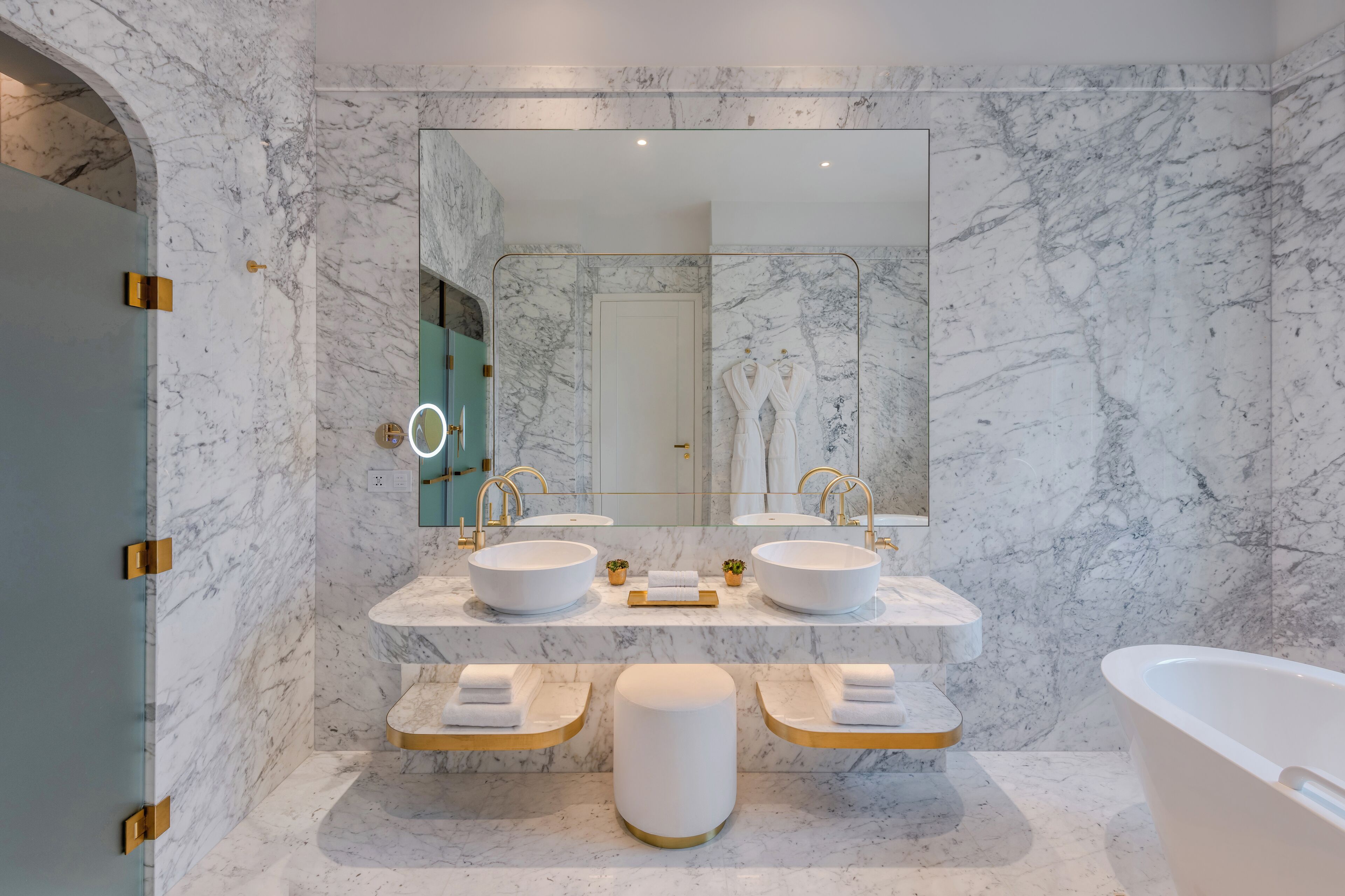 Un baño moderno con paredes de mármol, dos lavamanos, un espejo grande y una bañera.