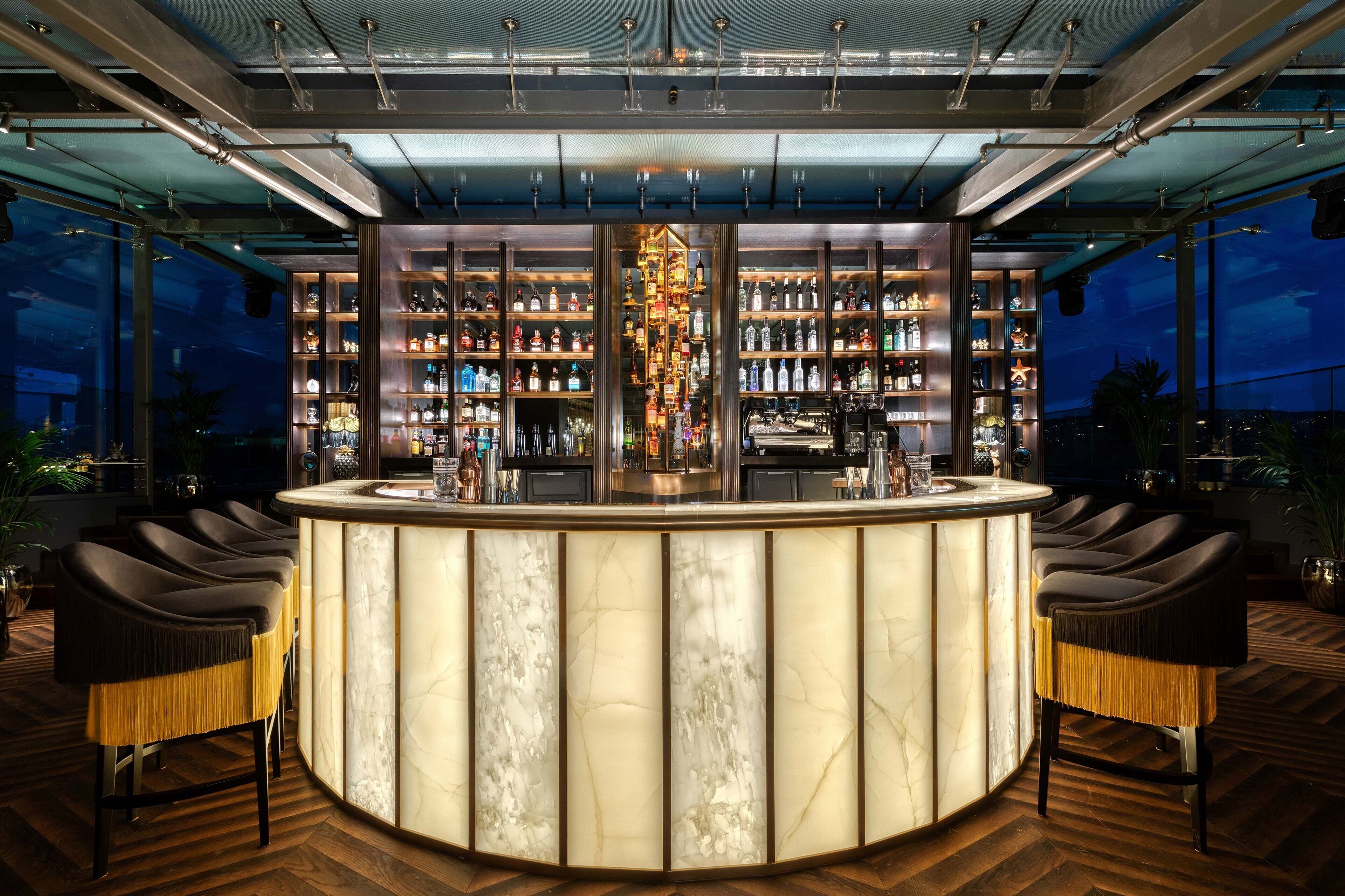 A bar with a marble countertop, multiple shelves of bottles, and two bar stools.