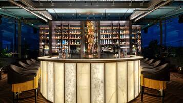 A bar with a marble countertop, multiple shelves of bottles, and two bar stools.