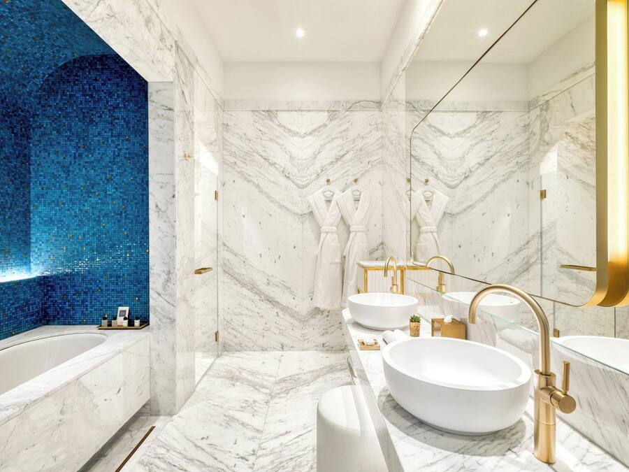 A modern bathroom with a large bathtub, two sinks, and a blue mosaic wall.