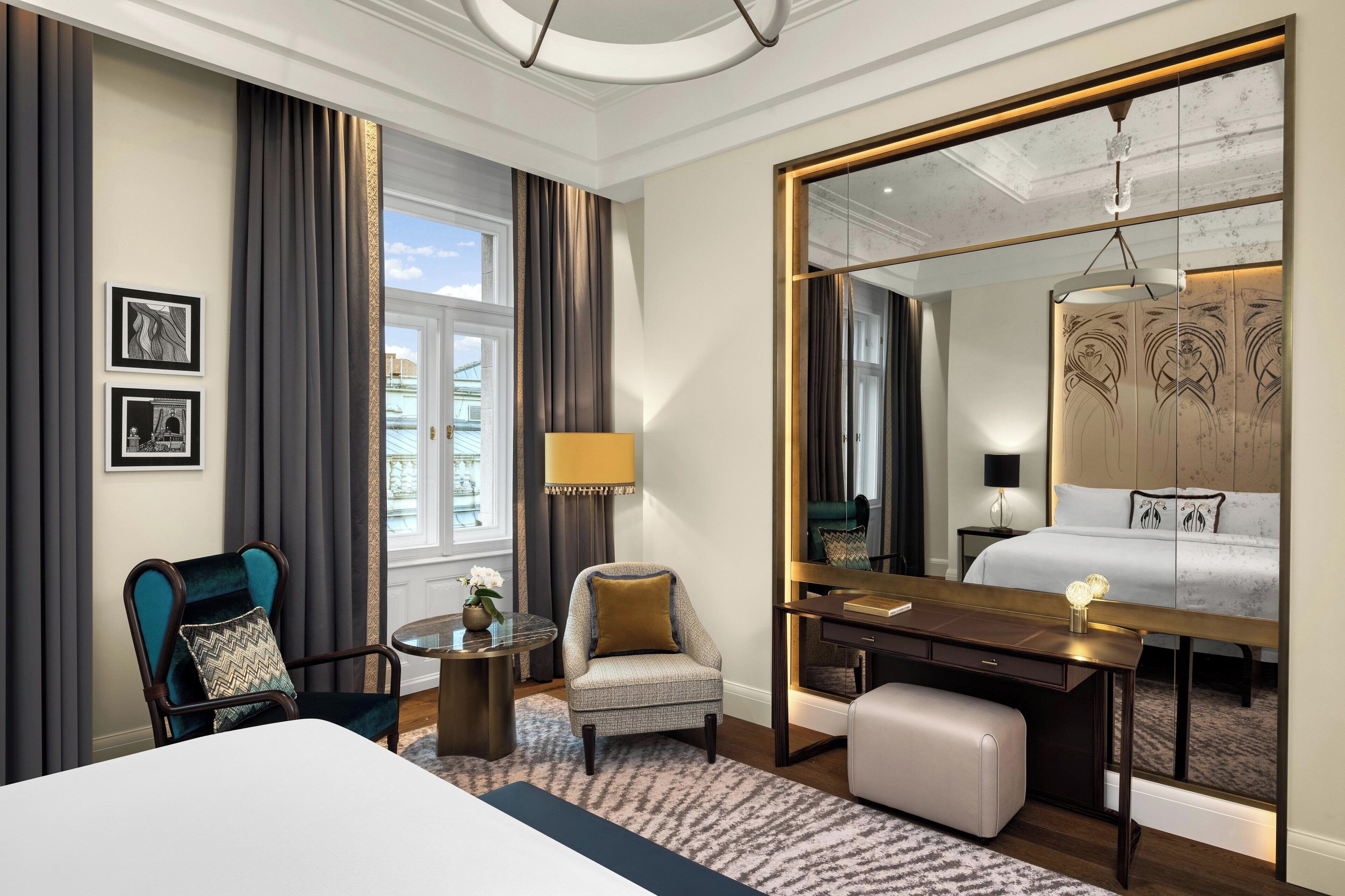 Une chambre d’hôtel avec un lit, un bureau, une chaise, une table ronde et un grand miroir.
