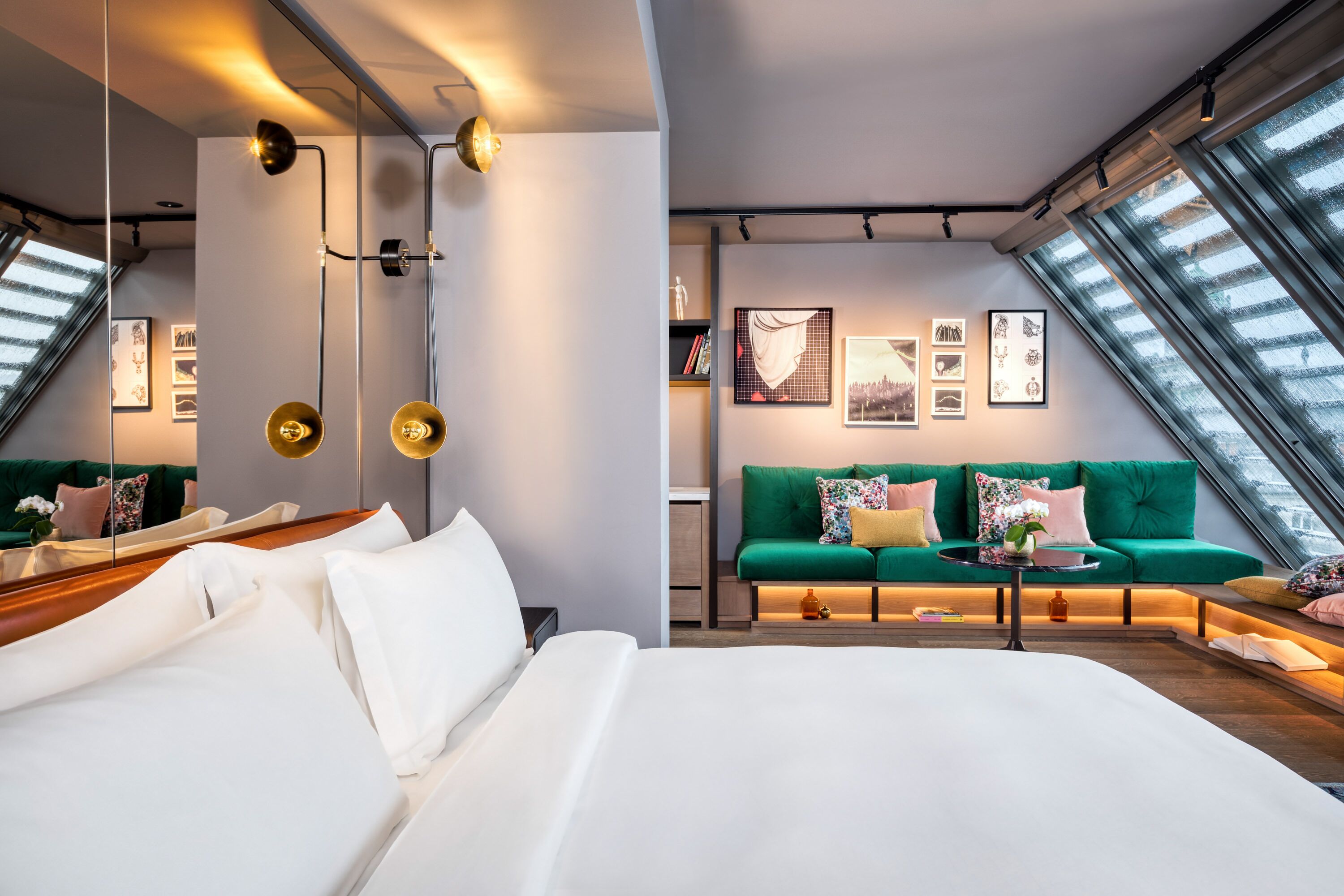 Une chambre d’hôtel moderne avec un grand lit, un canapé vert et une lucarne.