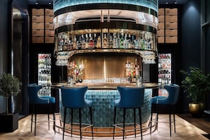 Un espace bar au design circulaire, avec de nombreuses étagères remplies de bouteilles et des tabourets de bar bleus.