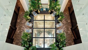 A spacious lobby with a central seating area, surrounded by potted plants and glass walls.