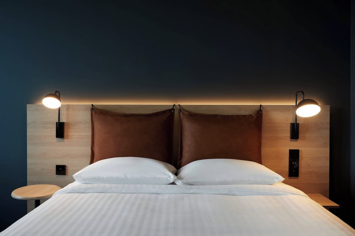 A modern bedroom with a wooden headboard, two bedside tables, and two wall-mounted lamps.