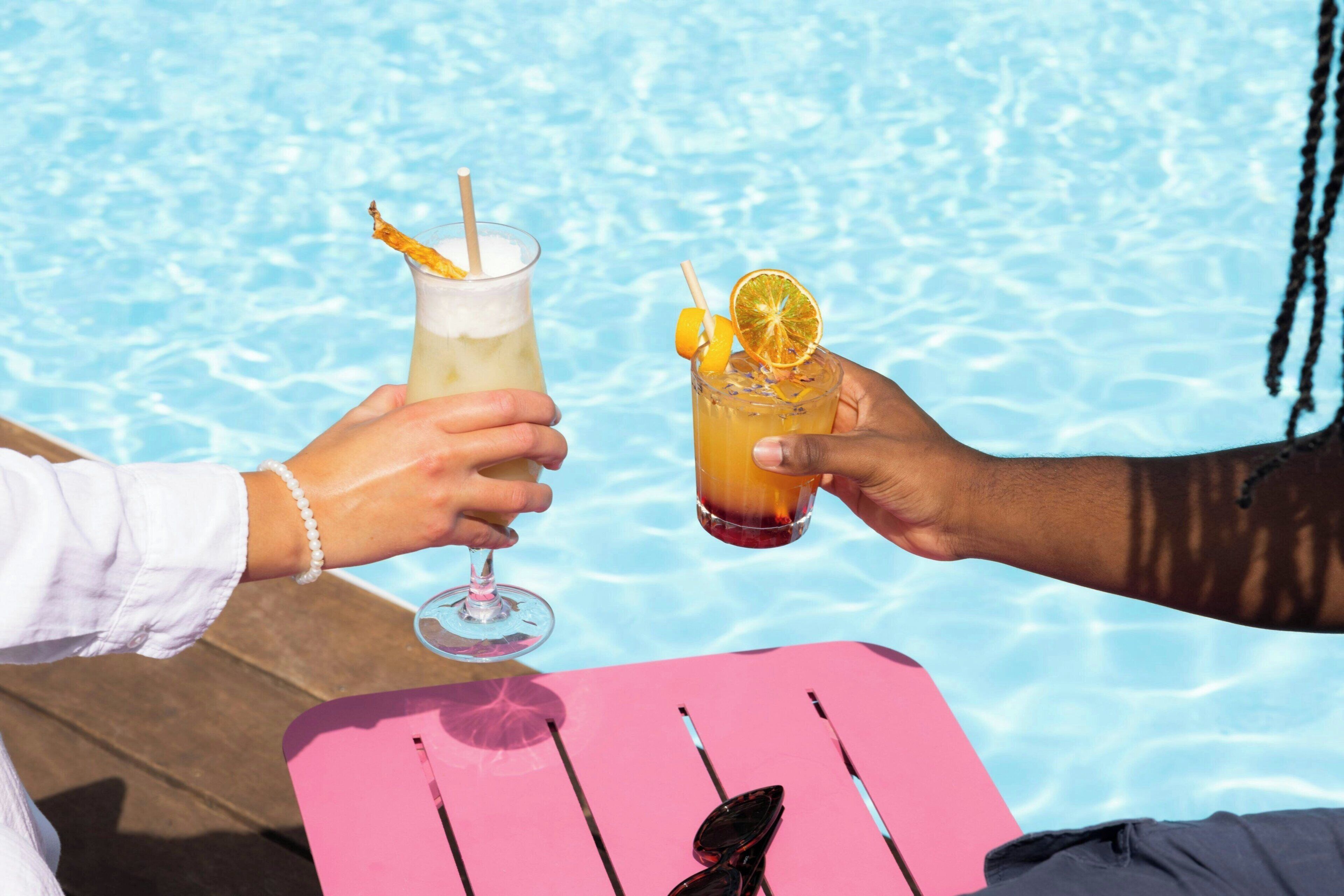 Dos personas brindando con bebidas junto a una piscina.