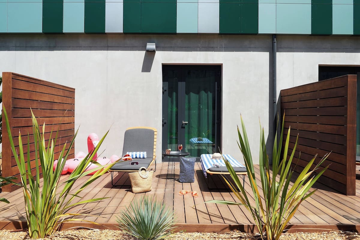 A deck with lounge chairs, a small table, and a door leading to a room.