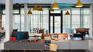 Een moderne woonkamer met een bank, een gitaar, een tafelvoetbalspel en grote ramen.
