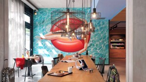 Een moderne eetruimte met een lange houten tafel, stoelen, een grote muurschildering en een bar voorzien van schappen.