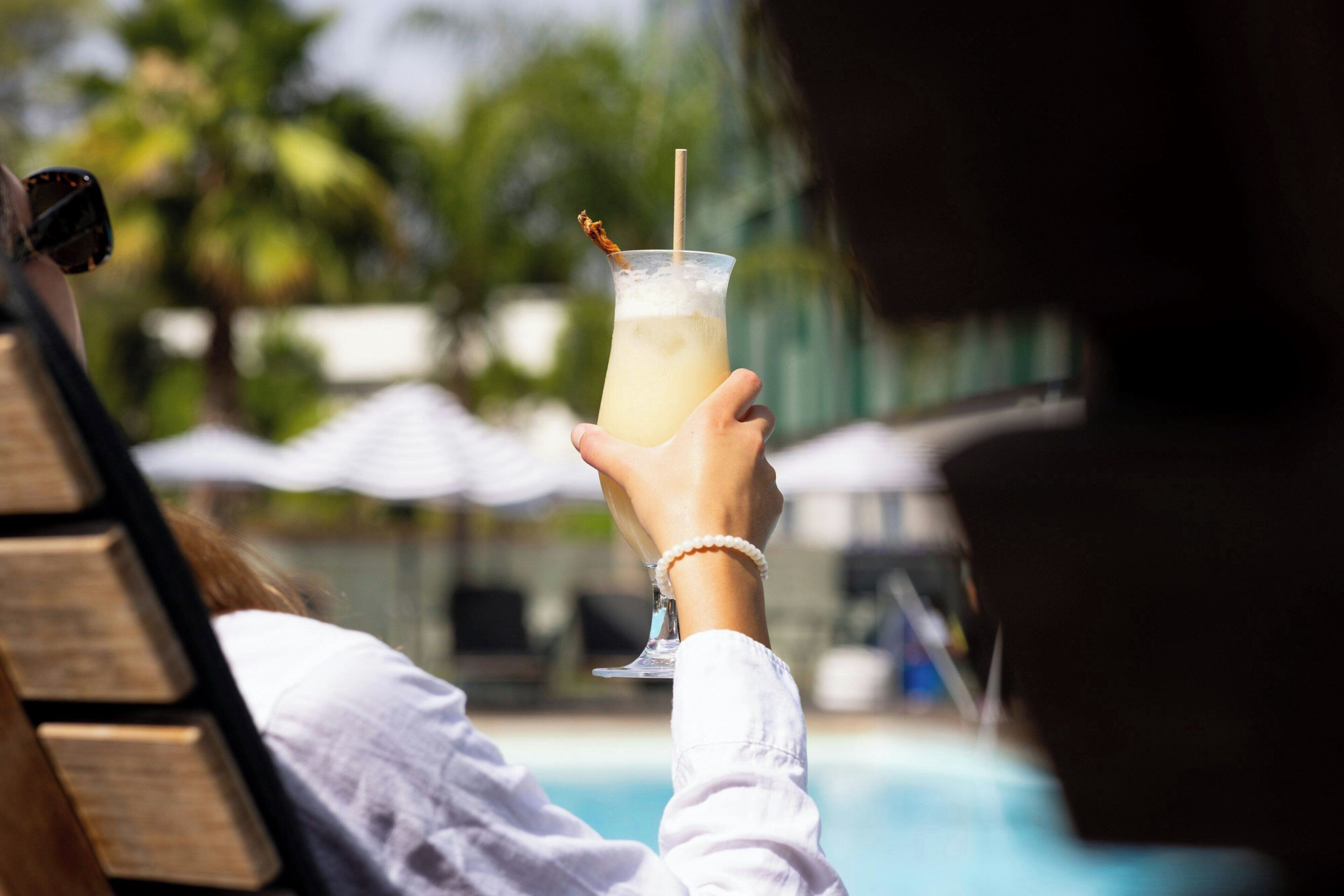Une personne, assise au bord d’une piscine, tient un verre avec une paille.