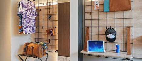 A room with a grid wall for hanging items, a laptop on a shelf, and a seating area with a chair and a small table.