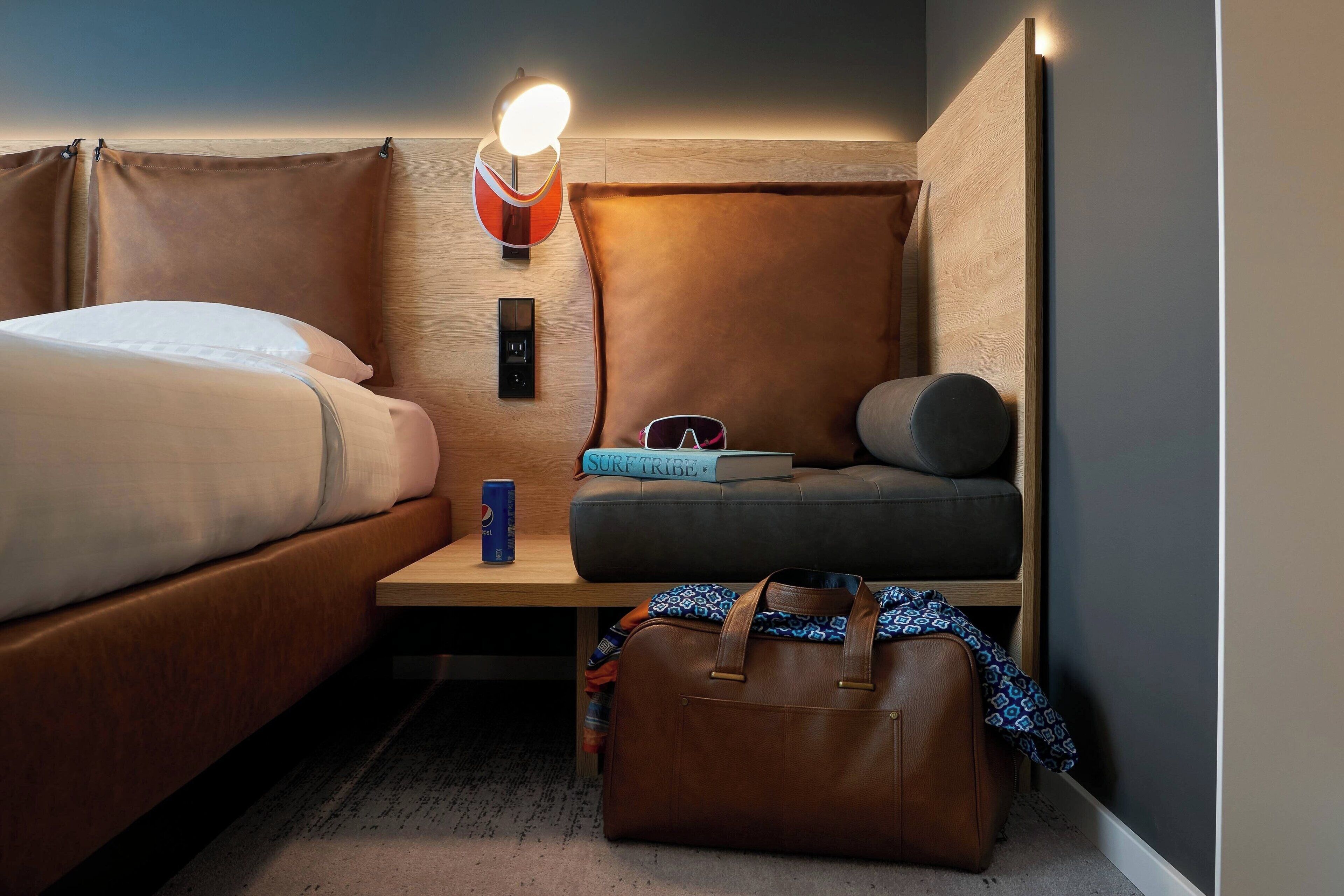 Une chambre d’hôtel de taille réduite, comprenant un lit, un canapé, un bureau et un espace pour une valise.
