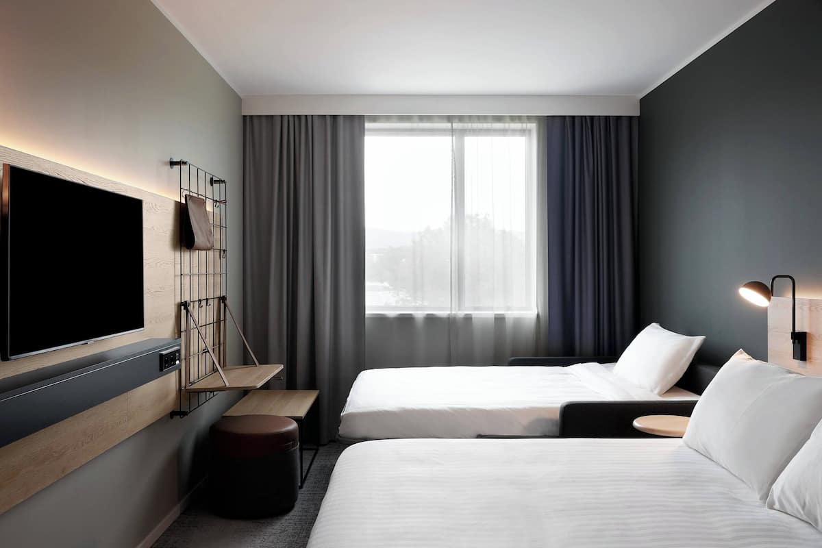 A modern hotel room with two beds, a flat-screen TV, a desk, and a large window with curtains.