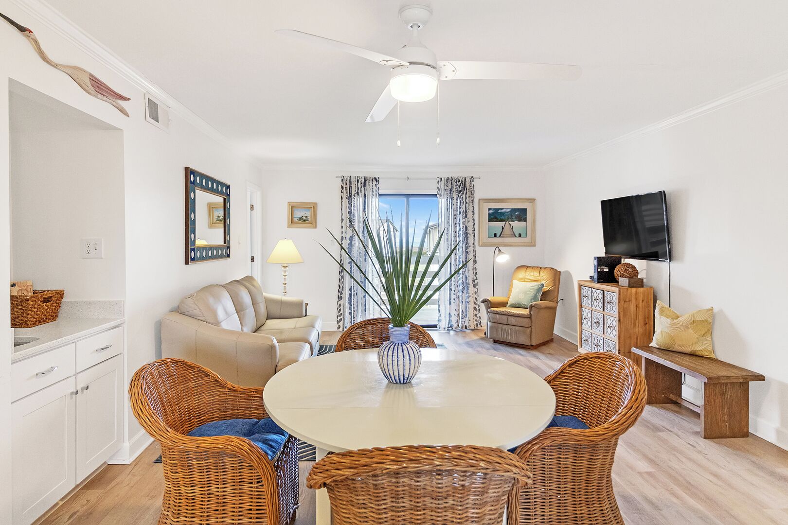 A modern living room with a dining table, wicker chairs, a sofa, a TV, and a ceiling fan.