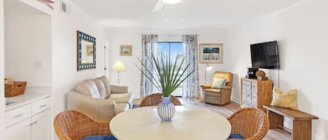 A modern living room with a dining table, wicker chairs, a sofa, a TV, and a ceiling fan.