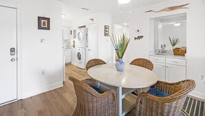 Een moderne keuken met witte apparaten, een eethoek met rieten stoelen en een plafondventilator.