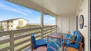 Een balkon met een houten vloer, een blauwe bank, twee stoelen en een kleine tafel.