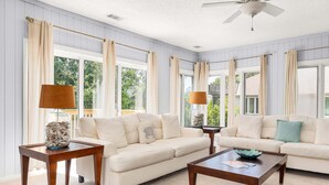 Ein Wohnzimmer mit zwei weißen Sofas, Holztischen und beigen Vorhängen.