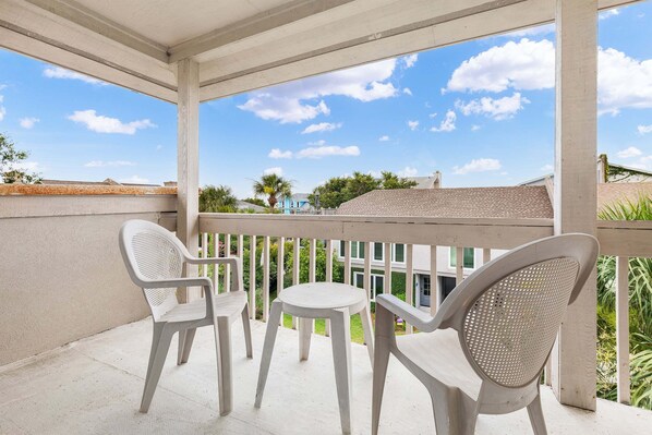 A balcony with two chairs and a small table, overlooking a residential area with houses and greenery. - Tybee Townhome: Ocean Views & Private Path to the Beach (Tybee Island)