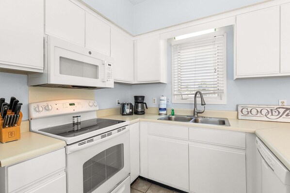 A kitchen with white cabinets, a microwave, a stove, a sink, and a coffee maker. - Tybee Townhome: Ocean Views & Private Path to the Beach (Tybee Island)