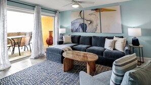 A modern living room with a sectional sofa, a coffee table, and a dining area with a table and chairs. - South Beach Escape | Ocean Views + Walkable Fun (Tybee Island)