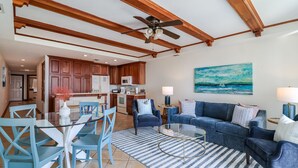 A spacious living area with a blue sofa, a glass coffee table, and a dining table with chairs. - Family-friendly Tybee Island condo w/ pools, ocean views & walk to beach (Tybee Island)