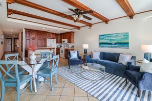 A spacious living area with a blue sofa, a glass coffee table, and a dining table with chairs. - Family-friendly Tybee Island condo w/ pools, ocean views & walk to beach (Tybee Island)
