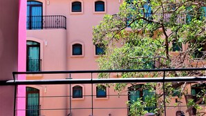 A balcony with two chairs and a table, overlooking a building with pink walls and multiple windows. - Hotel Mariachi by Kavia 5th Av (Playa del Carmen)