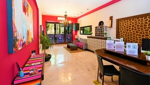 A modern reception area with a red and white color scheme, a chandelier, a sofa, a desk with informational cards, and a giraffe-patterned wall. - Hotel Mariachi by Kavia 5th Av (Playa del Carmen)