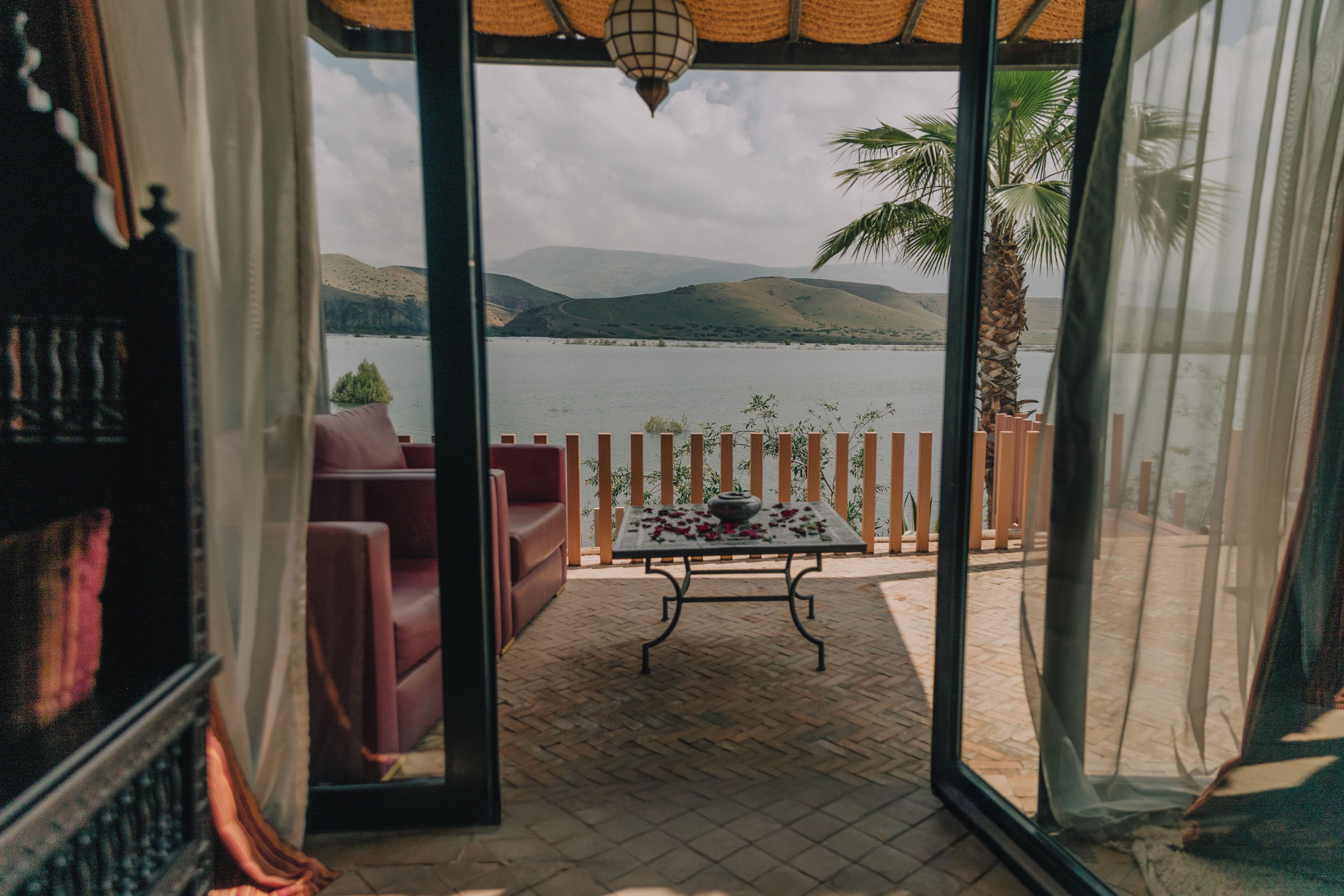 A room with a view of a lake and mountains through a glass door.