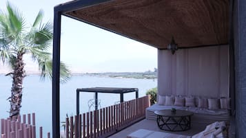 A balcony with a view of a body of water, a palm tree, and a seating area with cushions and a table.