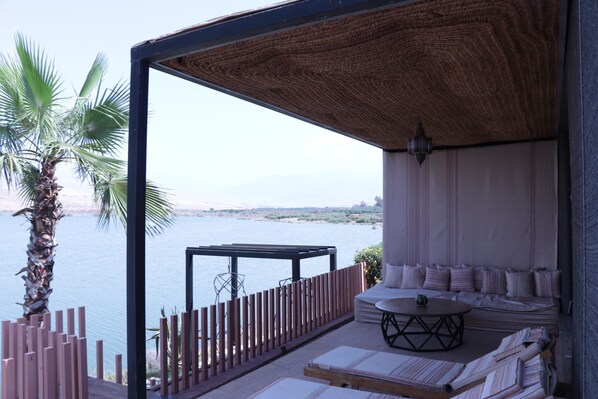 Un balcón con vista al agua, una palmera y una zona de estar con cojines y una mesa.