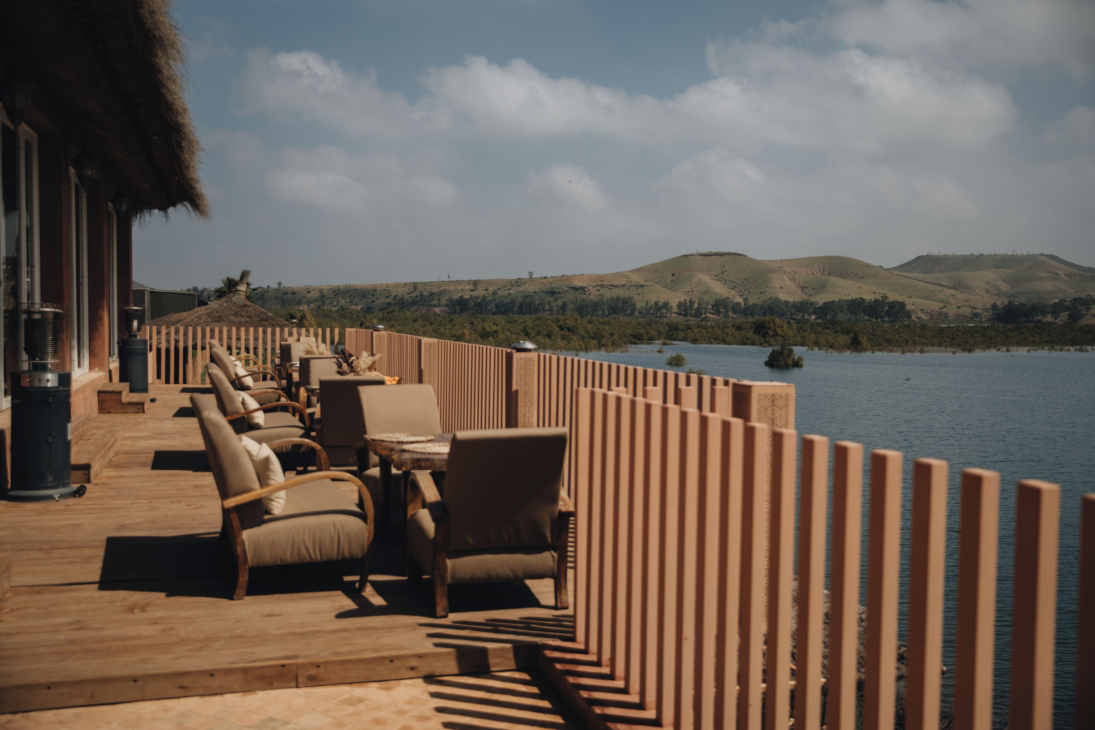 A wooden deck with outdoor seating, overlooking a body of water and hills.