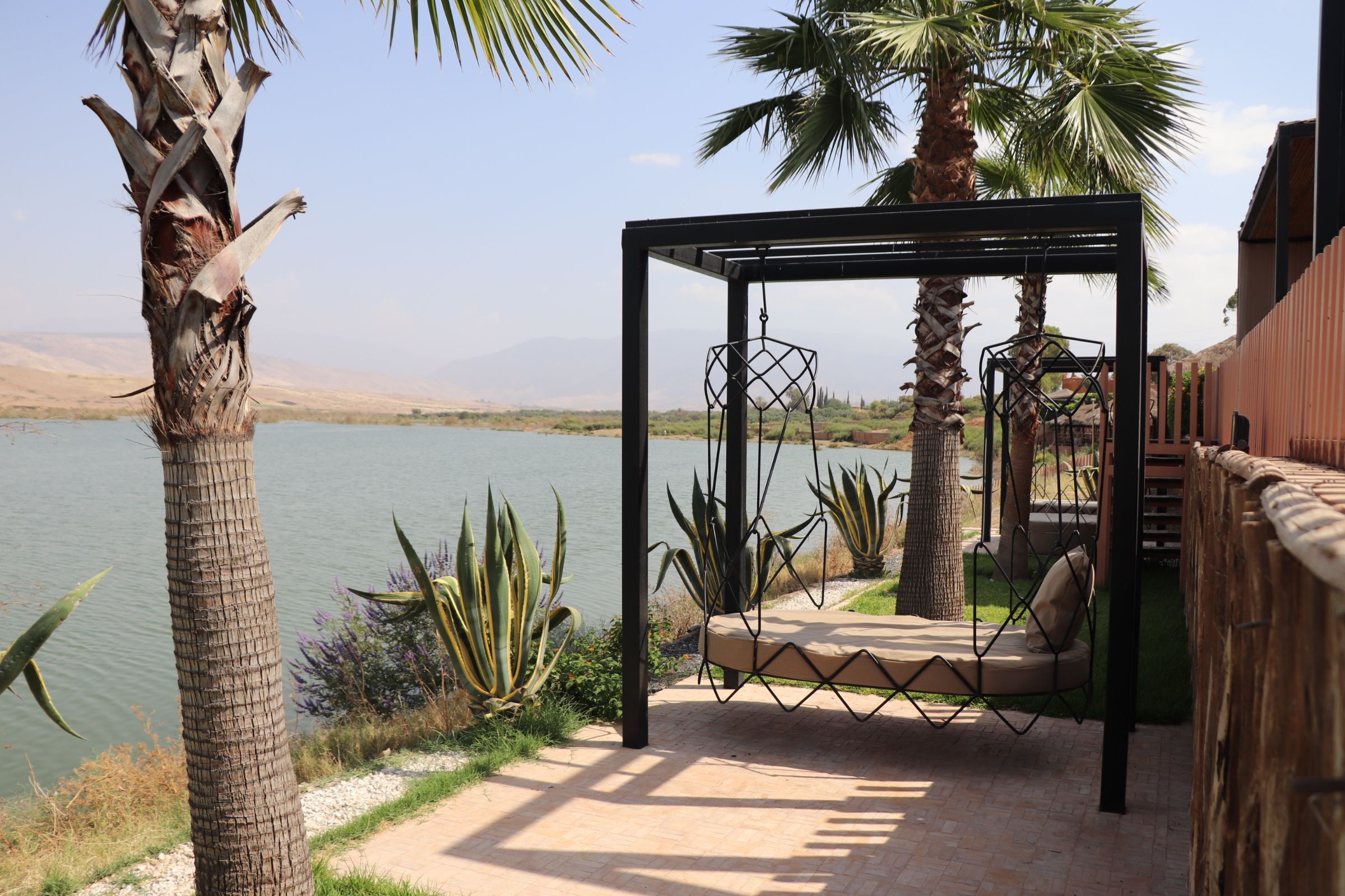 A patio with a swing chair, palm trees, and a view of a lake.