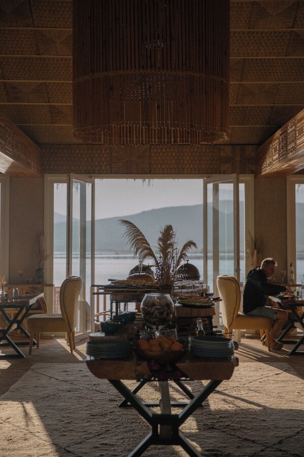 A dining area with a table set for two, overlooking a body of water and mountains. - Kalyptus Luxury Camp (Lalla Takarkoust)