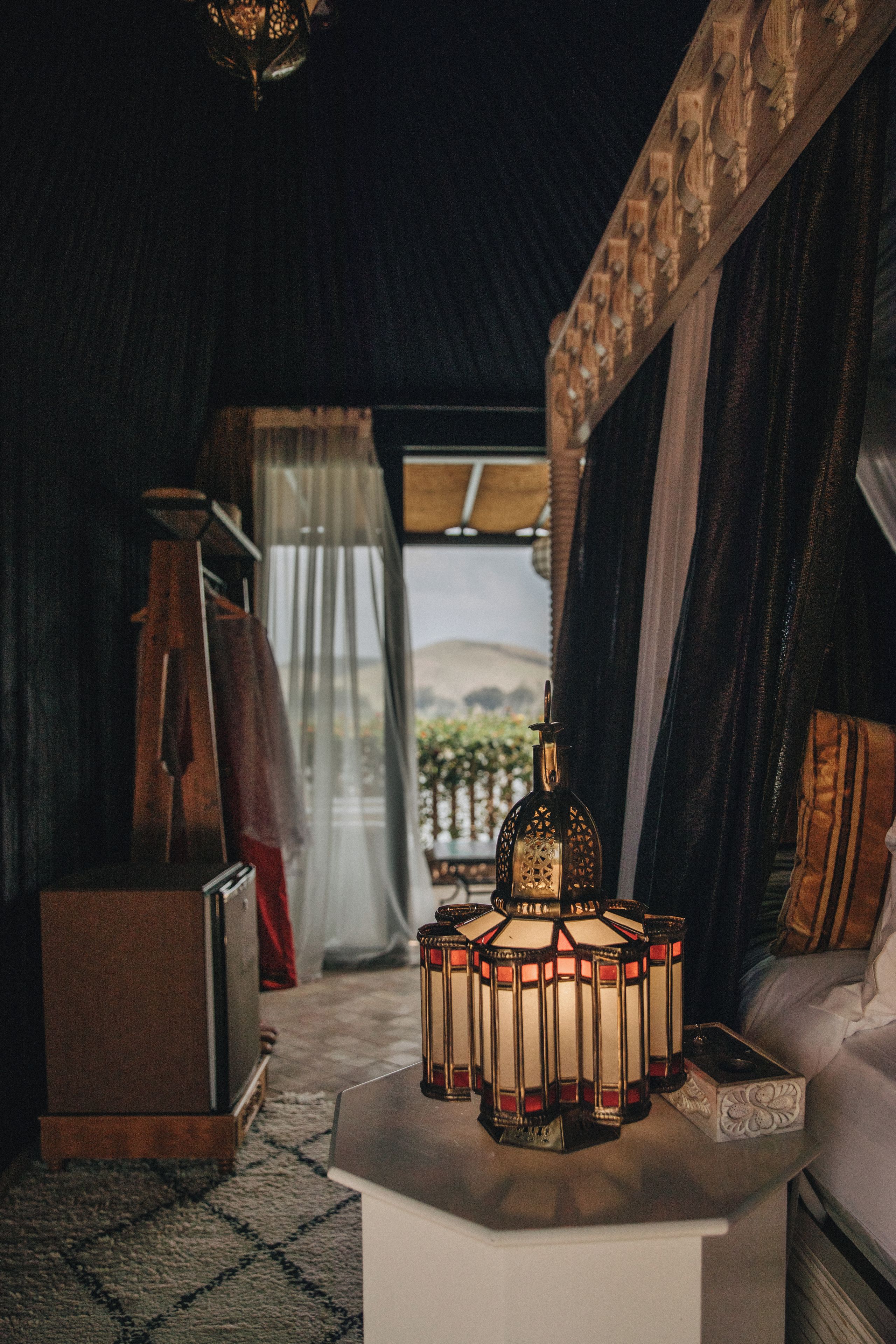 Un interior acogedor con un farol decorativo, un cofre de madera y vistas al exterior a través de una ventana.