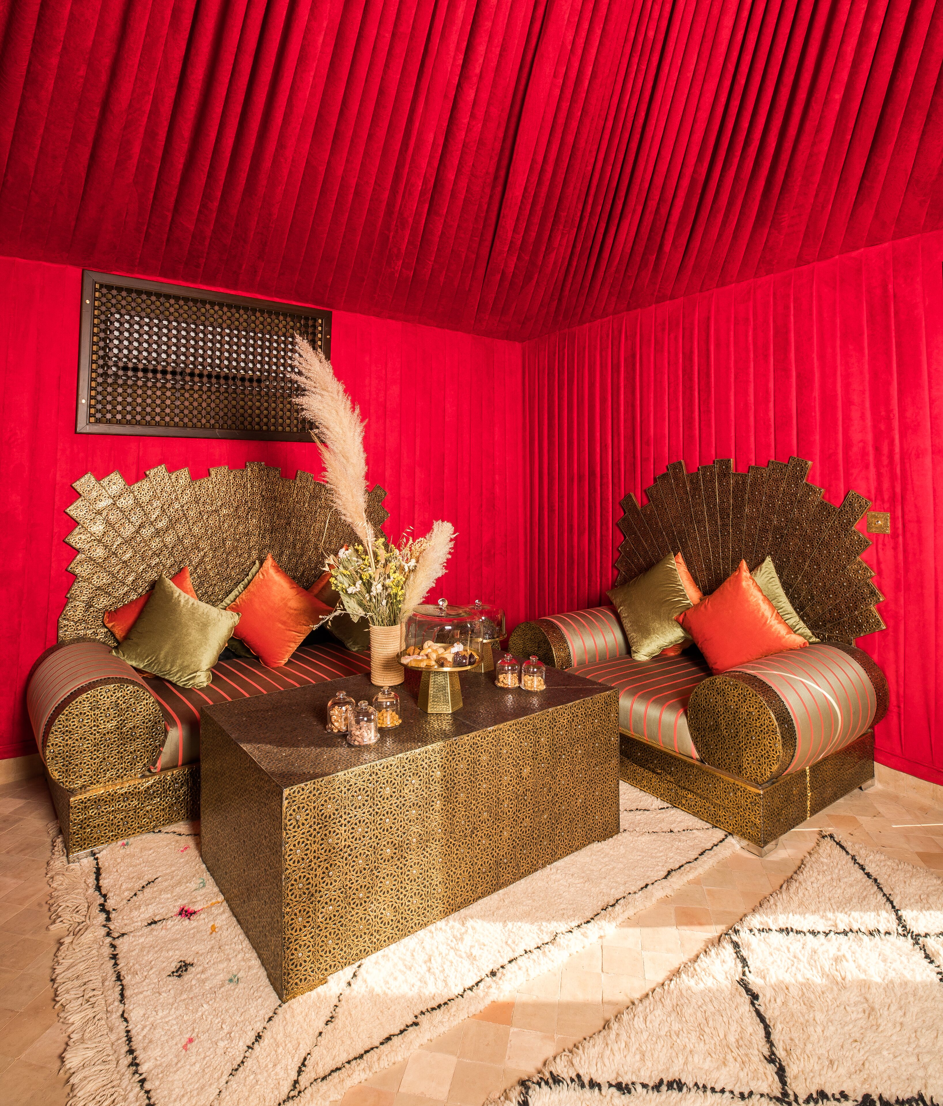 Una stanza con tenda rossa sullo sfondo, divano con motivi decorativi, tavolino da caffè al centro e cuscini decorativi.
