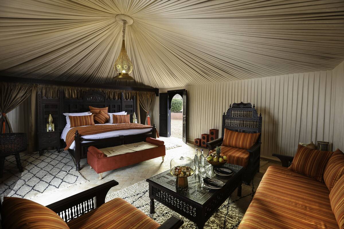 Um quarto tipo tenda luxuoso, com uma cama, sofás, uma mesa de centro e uma gaiola decorativa.