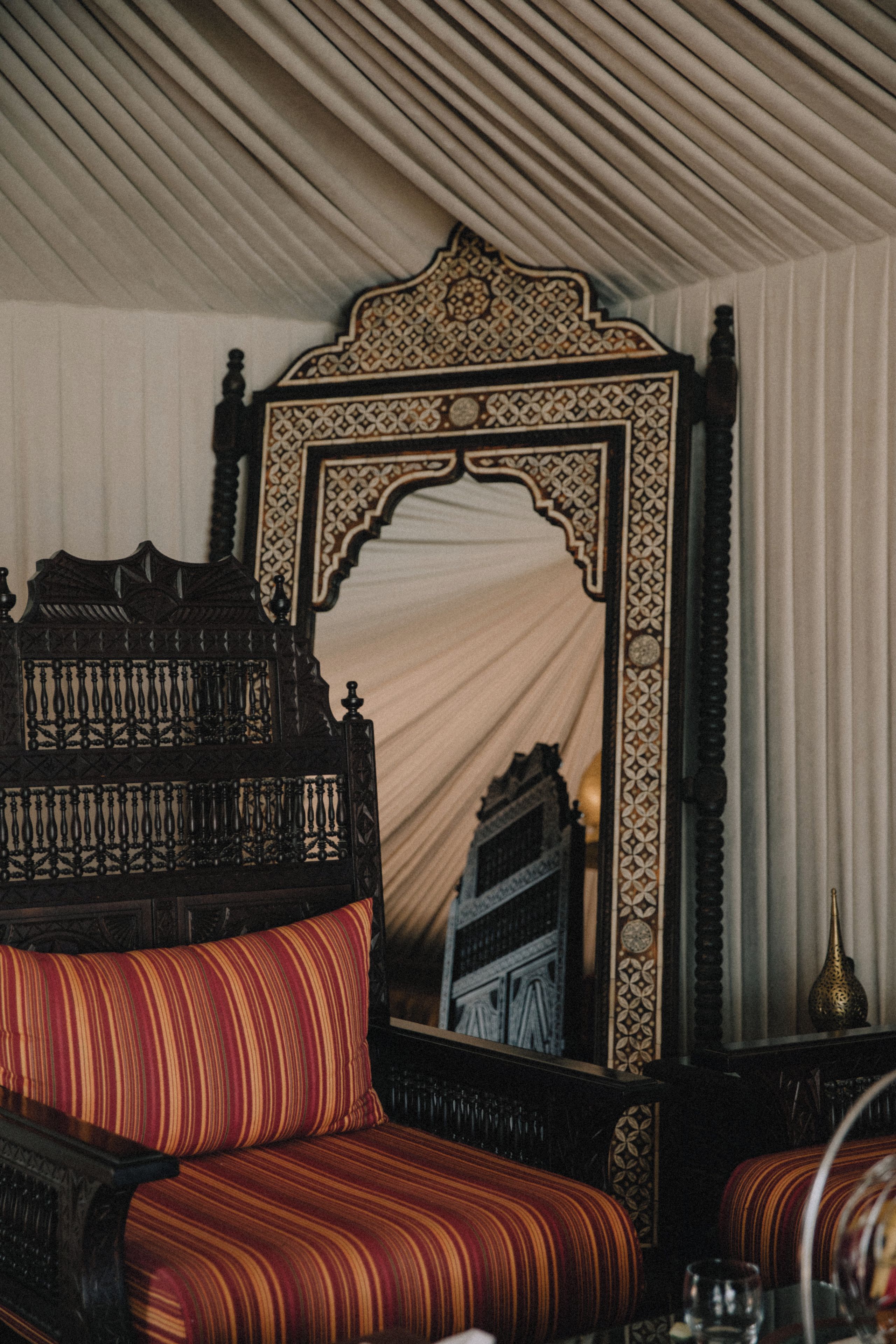 A room with a traditional sofa, a large ornate mirror, and a patterned wall.