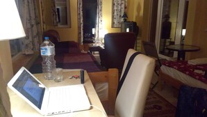 A hotel room with a bed, a desk with a laptop, a chair, a table, a lamp, a bottle of water, and a glass. - Immaculate 1-bed House in Nagymaros (Nagymaros)