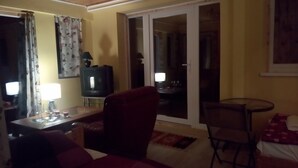 A living room with a sofa, a TV on a stand, a table with a lamp, and a chair. - Immaculate 1-bed House in Nagymaros (Nagymaros)