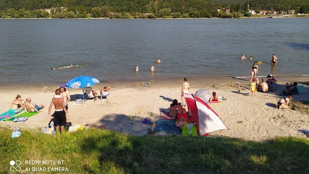 A beach with people sunbathing and swimming, a tent, and a clear view of the water and hills in the background. - Immaculate 1-bed House in Nagymaros (Nagymaros)