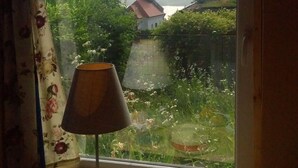 A table with a lamp, a cake, and a plate with food items. A window reveals a view of a building with a dome and greenery outside. - Immaculate 1-bed House in Nagymaros (Nagymaros)