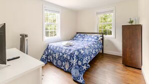 A bedroom with a bed, a TV, a radiator, and two windows. - Dennis Beach House - Walk to Beach - Pet Friendly (Dennis)