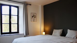 A bedroom with a large bed, a window with curtains, a wall-mounted light, and a framed picture. - Charming vacation home with terrace and garden (Sart-en-Fagne)