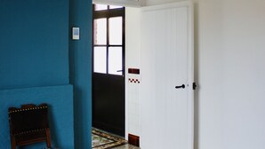 A hallway with a blue wall, a patterned floor, a wooden chair, and a white door. - Charming vacation home with terrace and garden (Sart-en-Fagne)