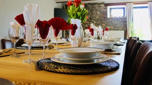 A dining table set with white napkins, red flower arrangements, and clear glassware. - Charming vacation home with terrace and garden (Sart-en-Fagne)