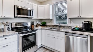 A modern kitchen with white cabinetry, stainless steel appliances, a granite countertop, and a window with blinds.