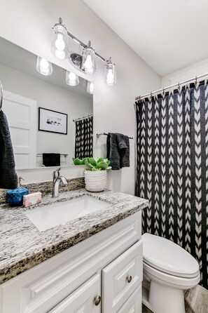 A bathroom with a granite countertop, white cabinets, a white sink, a mirror with lights, a black and white patterned shower curtain, and a toilet. - The Pine House: Unit A near 6th Ave, UPS, UW, and Point Ruston (Tacoma)