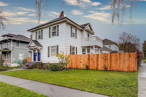 A two-story house with a front porch, a wooden fence, and a well-maintained lawn. - The Pine House: Unit A near 6th Ave, UPS, UW, and Point Ruston (Tacoma)